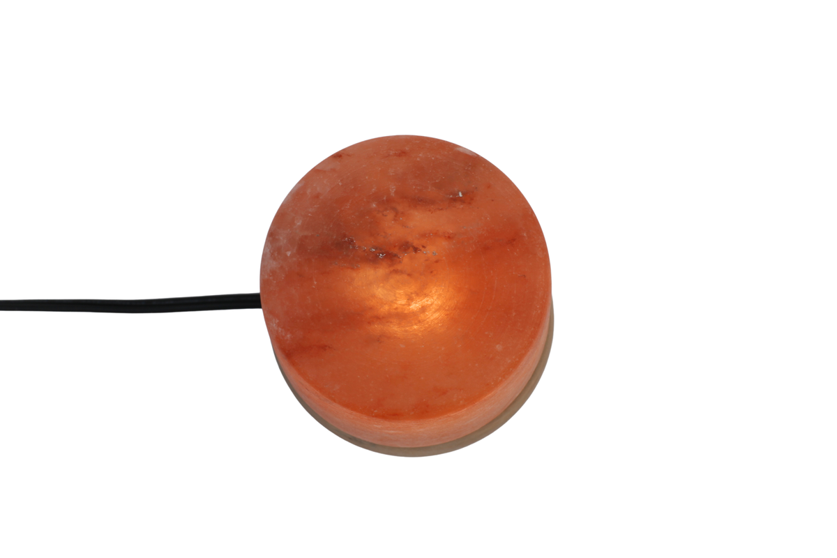 Round pink salt lamp object with a black cord on a white background